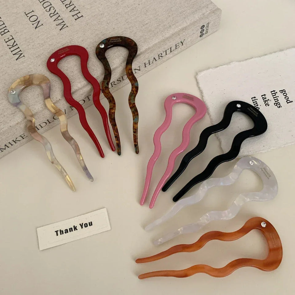 A collection of colorful wavy hair forks arranged on a surface with books. Secondary image