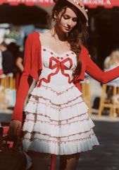 Close-up of a woman wearing a white tiered ruffle dress with red trim and a red cardigan.