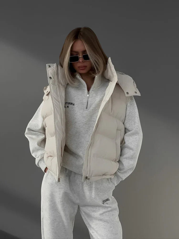 Woman wearing a cream puffer vest over a cream quarter-zip hoodie and cream joggers, with sunglasses and hands in pockets. Main image