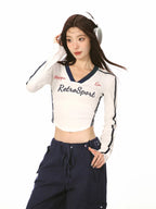 Woman wearing a white cropped long-sleeve shirt with navy trim and 'RetroSport' text, paired with navy cargo pants and white sneakers.
