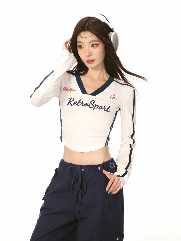 Woman wearing a white cropped long-sleeve shirt with navy trim and 'RetroSport' text, paired with navy cargo pants and white sneakers.