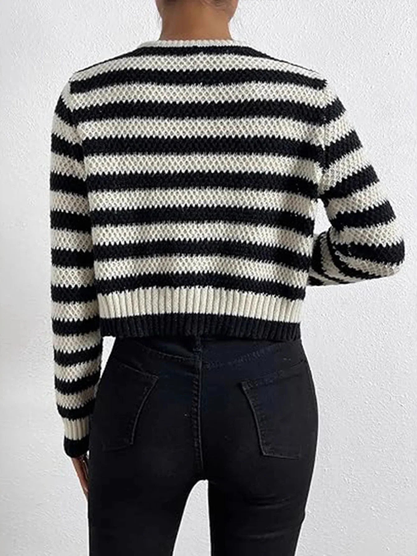 Back view of a woman wearing a black and white striped cropped knit cardigan and black jeans.