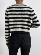 Back view of a woman wearing a black and white striped cropped knit cardigan and black jeans.