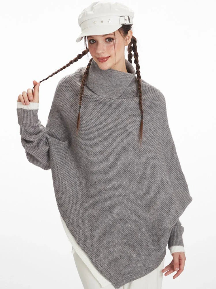 Close-up of a woman wearing a grey asymmetrical knit poncho with a turtleneck, holding the braid of her hair