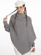 Close-up of a woman wearing a grey asymmetrical knit poncho with a turtleneck, holding the braid of her hair