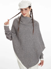 Close-up of a woman wearing a grey asymmetrical knit poncho with a turtleneck, holding the braid of her hair