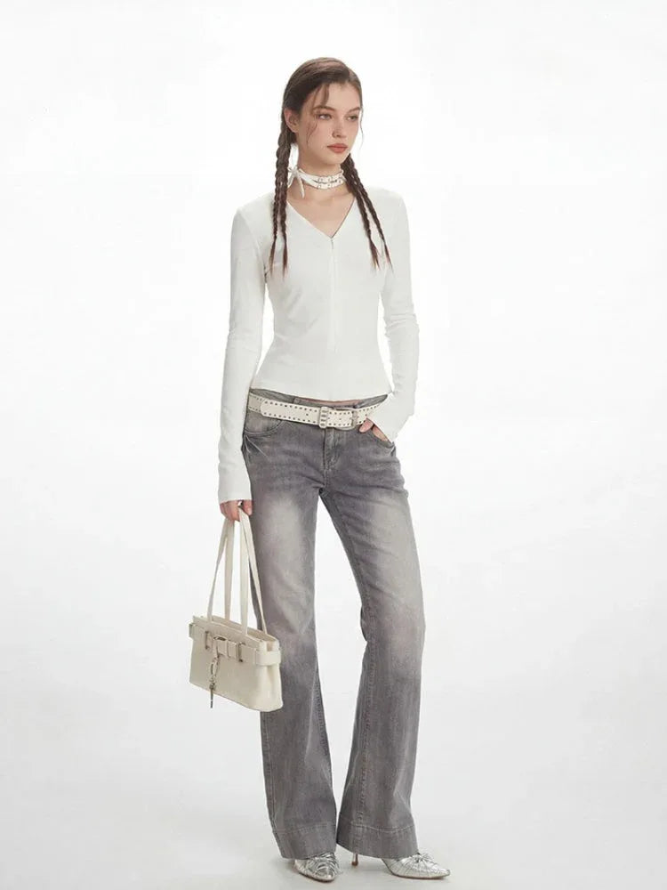 Model in a white long-sleeved ribbed V-neck top and grey flared jeans, holding a white shoulder bag.