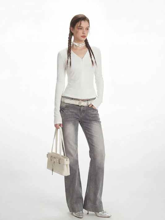 Model in a white long-sleeved ribbed V-neck top and grey flared jeans, holding a white shoulder bag.