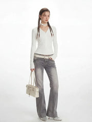 Model in a white long-sleeved ribbed V-neck top and grey flared jeans, holding a white shoulder bag.
