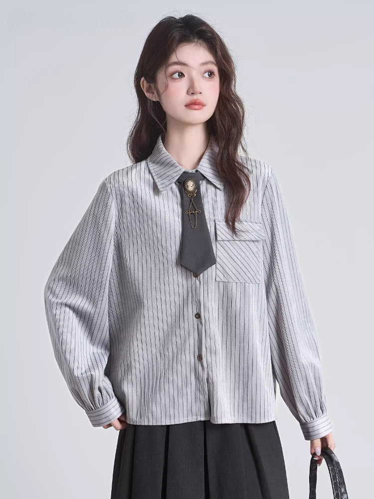 Close-up of a woman's torso wearing a grey pinstripe collared shirt with a dark tie and brooch.