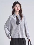 Close-up of a woman's torso wearing a grey pinstripe collared shirt with a dark tie and brooch.