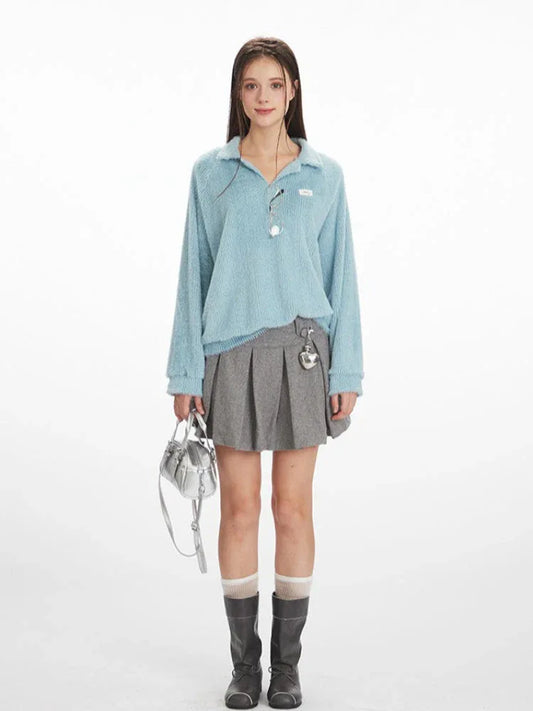Model wearing a light blue fuzzy knit collared v-neck sweater with a grey pleated mini skirt, white and grey striped socks, and black boots.