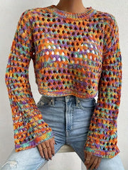 Woman sitting down wearing a multicolored open-knit cropped sweater and light-wash denim jeans.