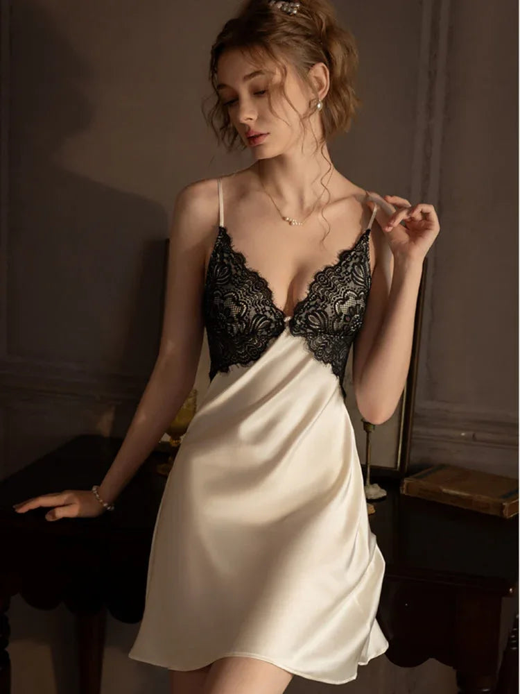 Woman wearing a cream-colored satin chemise with black lace trim, leaning on a table.