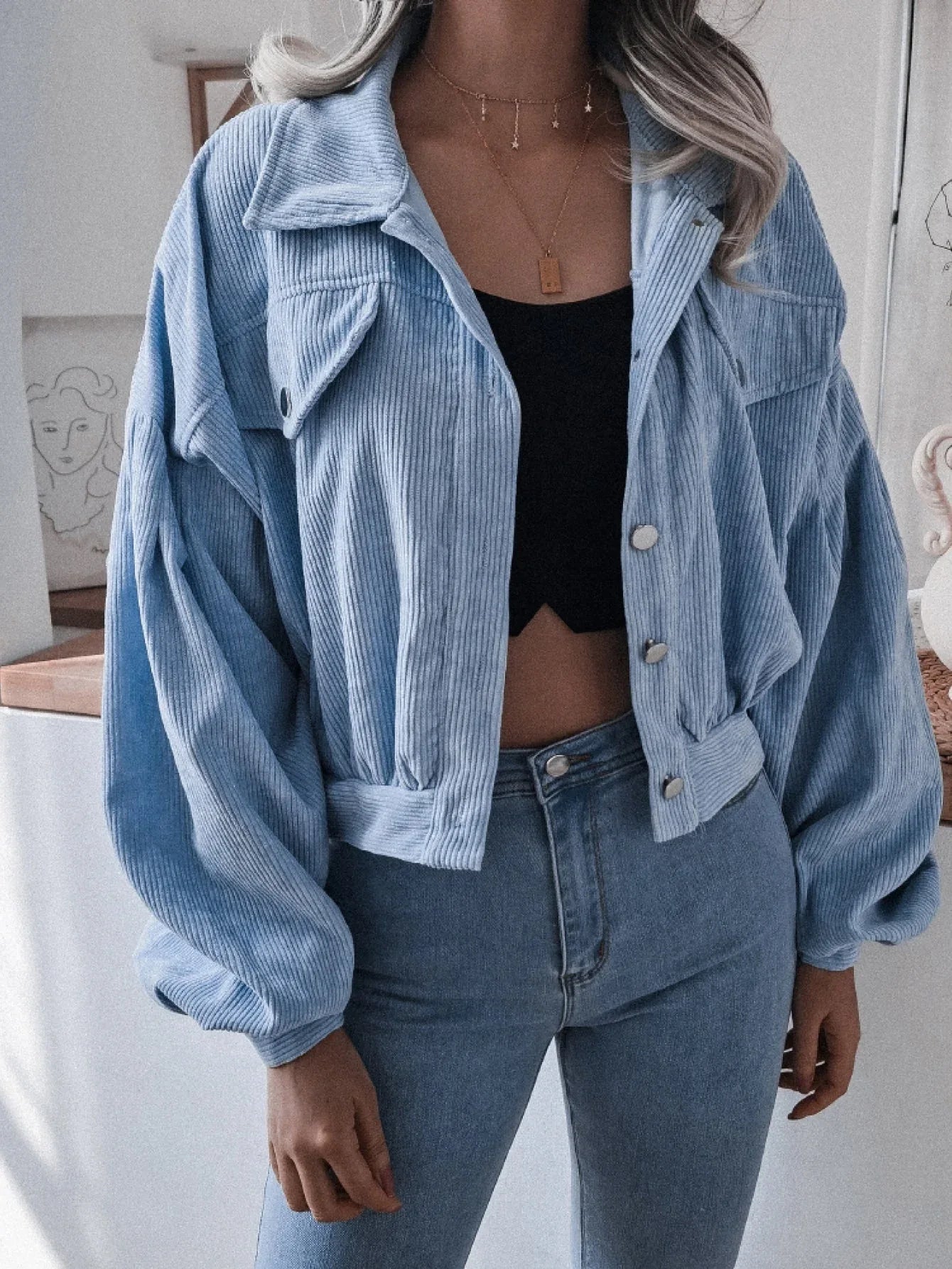 Woman wearing a light blue corduroy cropped jacket with balloon sleeves and a black crop top. Main image