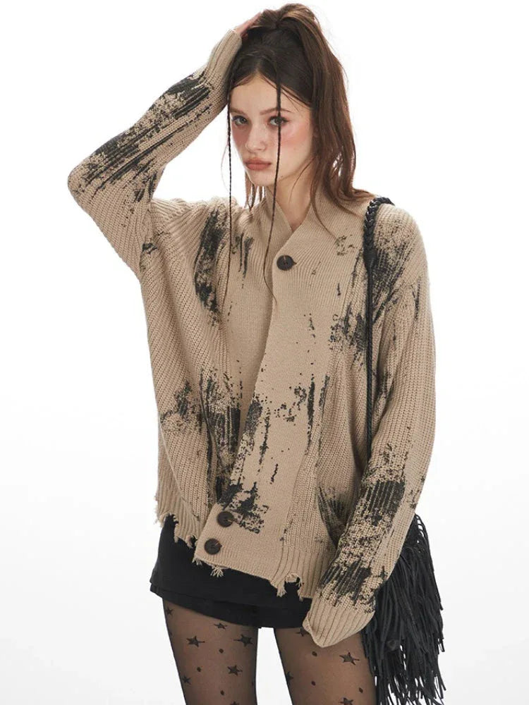 Close-up front view of a model wearing a distressed knit cardigan with a graphic print, showing the neckline and sleeve detail.