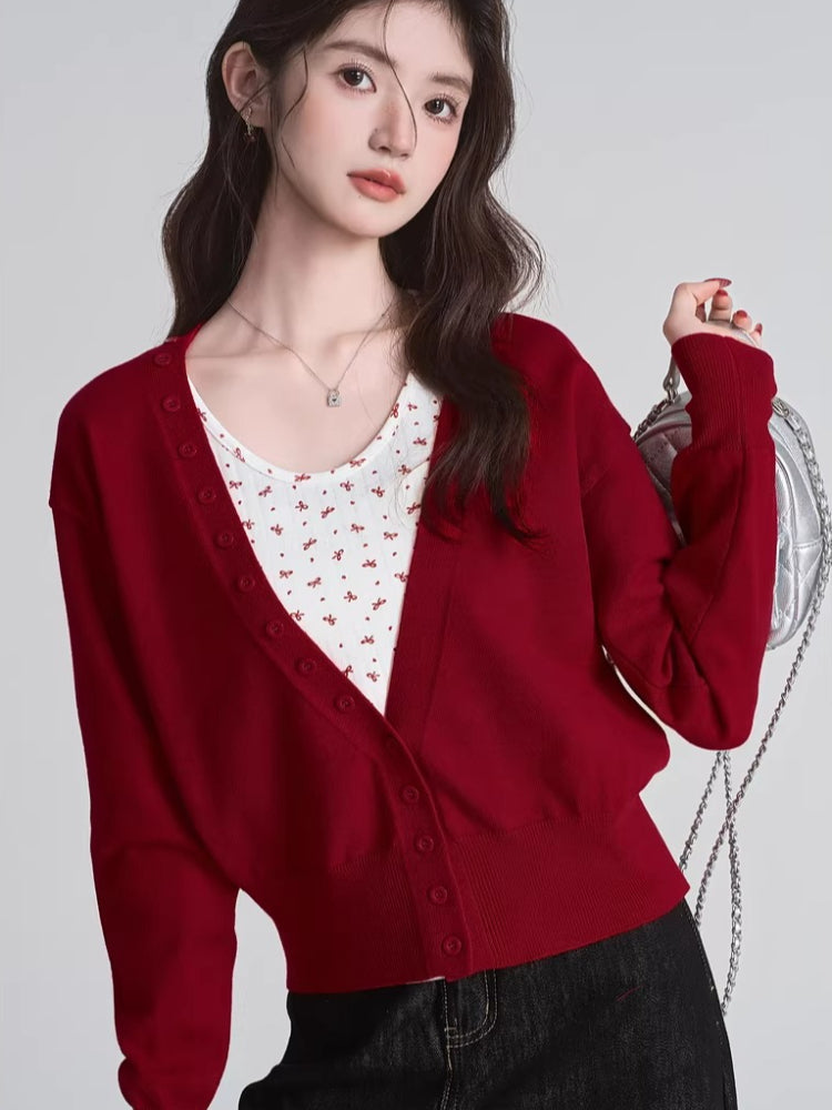 Close-up of a woman in a red V-neck cardigan and white floral tank top.