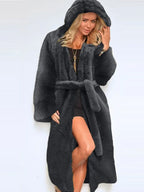 Woman wearing a long, dark grey faux fur coat with a hood and belt