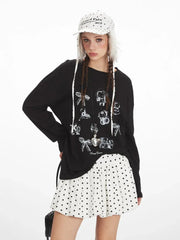 Front close-up of a young woman wearing a black long-sleeved graphic t-shirt with various charms printed on it. She is also wearing a white polka dot mini skirt and a white polka dot bucket hat with fur trim.