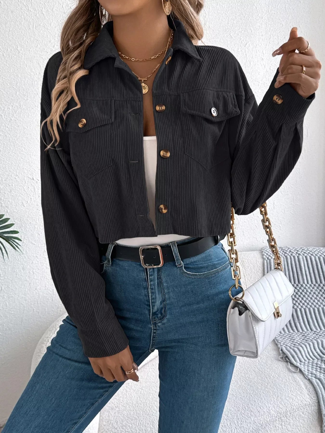 Woman wearing a black corduroy cropped jacket over a white tank top and blue jeans, holding a handbag.