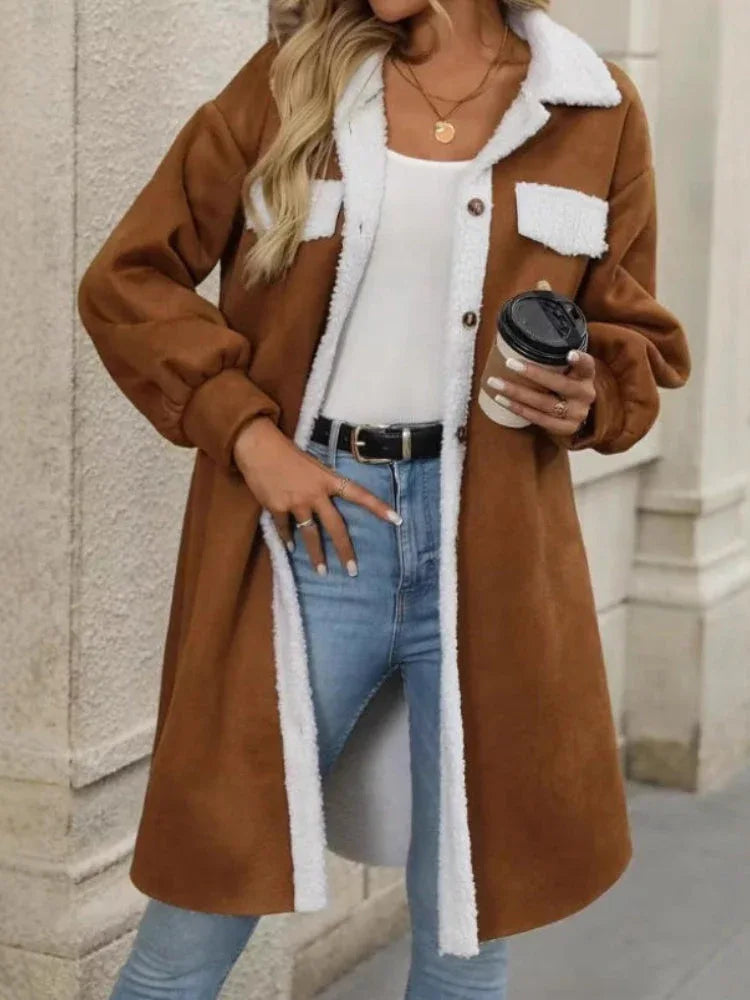 Woman in a brown fleece jacket with white sherpa trim, blue jeans, and a black belt, holding a coffee cup.