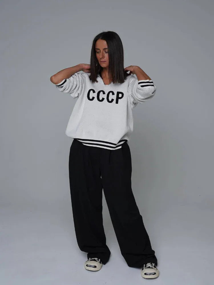 Woman wearing a white CCCP knit sweater with black stripes on the cuffs and hem, and black wide-leg pants.