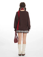 Back view of a woman wearing a brown knit sweater with a teddy bear graphic and a red scarf, paired with a patterned skirt and leg warmers