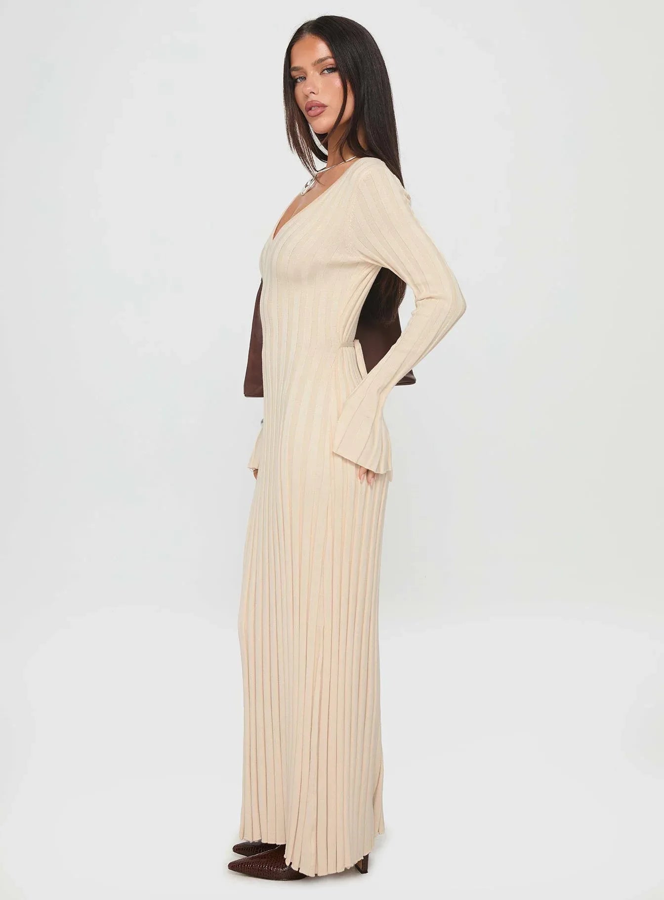 Side profile of a woman showcasing a cream ribbed knit maxi dress with a flattering silhouette and long sleeves.