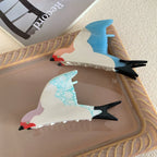 Two bird-shaped hair clips, one with blue wings and the other with blue-veined white wings, displayed on a tray.