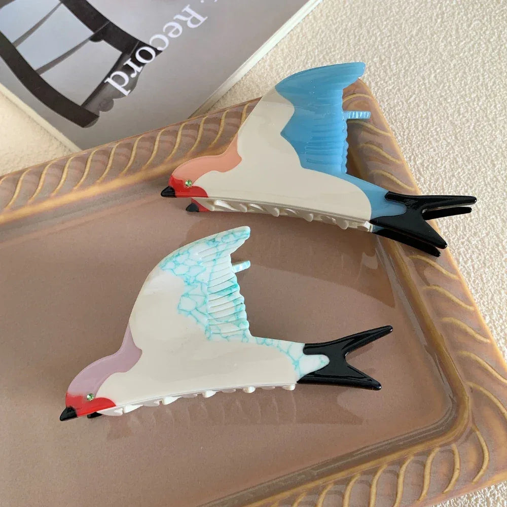 Two bird-shaped hair clips, one with blue wings and the other with blue-veined white wings, displayed on a tray.