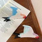 Two bird-shaped hair clips, one with blue wings and the other with blue-veined white wings, resting on an open book.