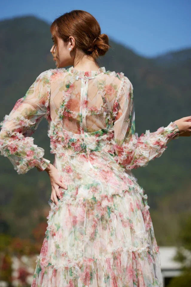 Back view of a woman wearing a floral print chiffon gown with tiered ruffles and bishop sleeves, showcasing the open back detail.