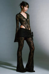 Full body shot of a model in a black lace bodysuit, mini skirt, and flared pants.