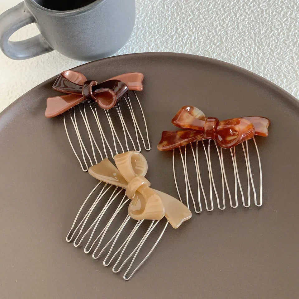 Three bow hair combs in varying shades of brown and tortoiseshell on a dark brown plate. Secondary image