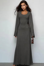 Woman wearing a long-sleeved, ribbed maxi dress with bell sleeves and a square neckline in a charcoal gray color, holding a small brown handbag.