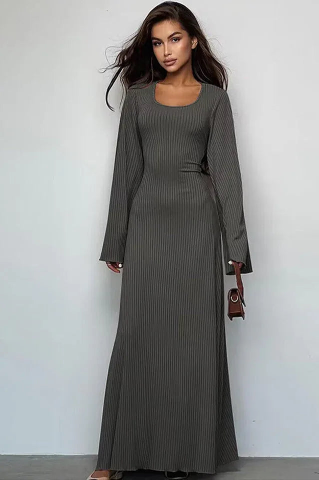 Woman wearing a long-sleeved, ribbed maxi dress with bell sleeves and a square neckline in a charcoal gray color, holding a small brown handbag.