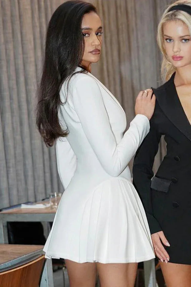 Woman in a white blazer dress with a pleated skirt, standing next to another woman in a black blazer.