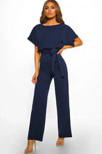 Woman wearing a navy blue wide leg jumpsuit with a tie waist and boat neck