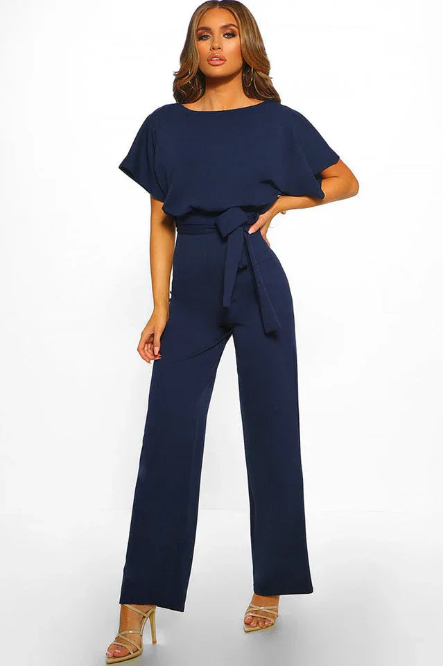 Woman wearing a navy blue wide leg jumpsuit with a tie waist and boat neck