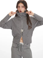 Woman zipping up a grey knit jacket, revealing a glimpse of white undergarment.