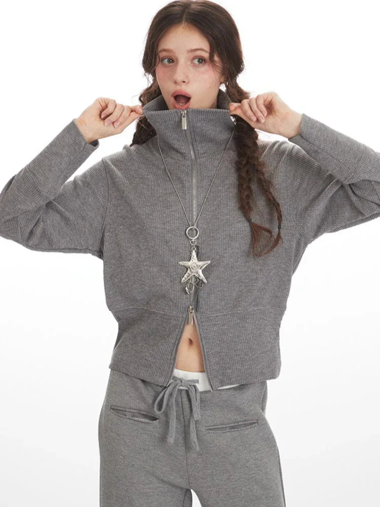 Woman zipping up a grey knit jacket, revealing a glimpse of white undergarment.