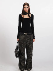 Woman in black long-sleeve top and camouflage cargo pants, holding a black handbag.