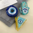 A flat lay of three evil eye accessories and a grey garment, with a piece of text in the background.