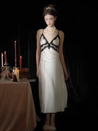 Woman standing in a white satin slip dress with black lace trim, pearl necklace, and fur stole.