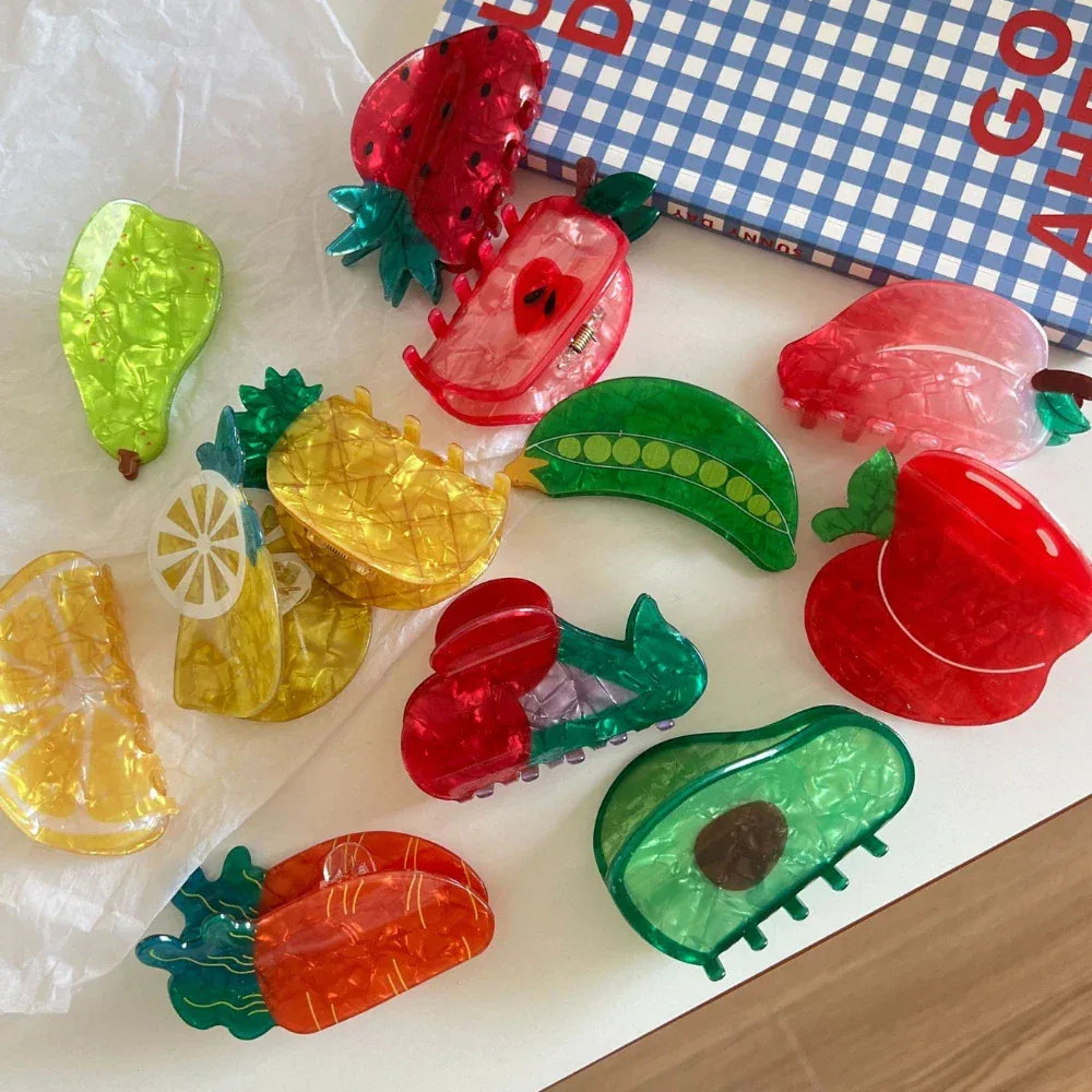 A collection of fruit-shaped hair clips including strawberries, apples, pears, pineapples, lemons, avocados, carrots, peas, and cherries.