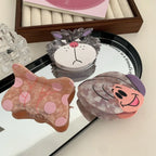 Three decorative hair clips, including a butterfly, a cat face, and a snail, displayed on a mirror.