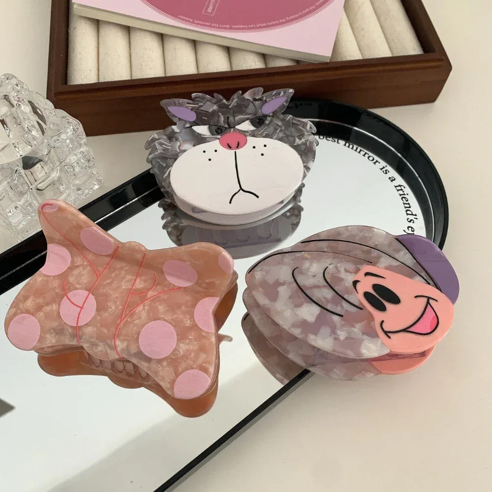 Three decorative hair clips, including a butterfly, a cat face, and a snail, displayed on a mirror.