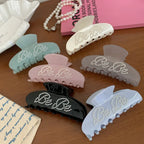 A collection of colorful claw clips, each featuring "Be Be" lettering with pearl-like studs, arranged on a wooden surface.