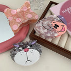 Close-up view of three decorative hair clips: a butterfly, a cat, and a snail, on a reflective surface.