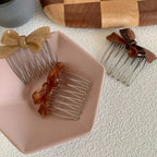 Three bow hair combs in beige, tortoiseshell, and brown arranged on a pink dish and white textured surface.